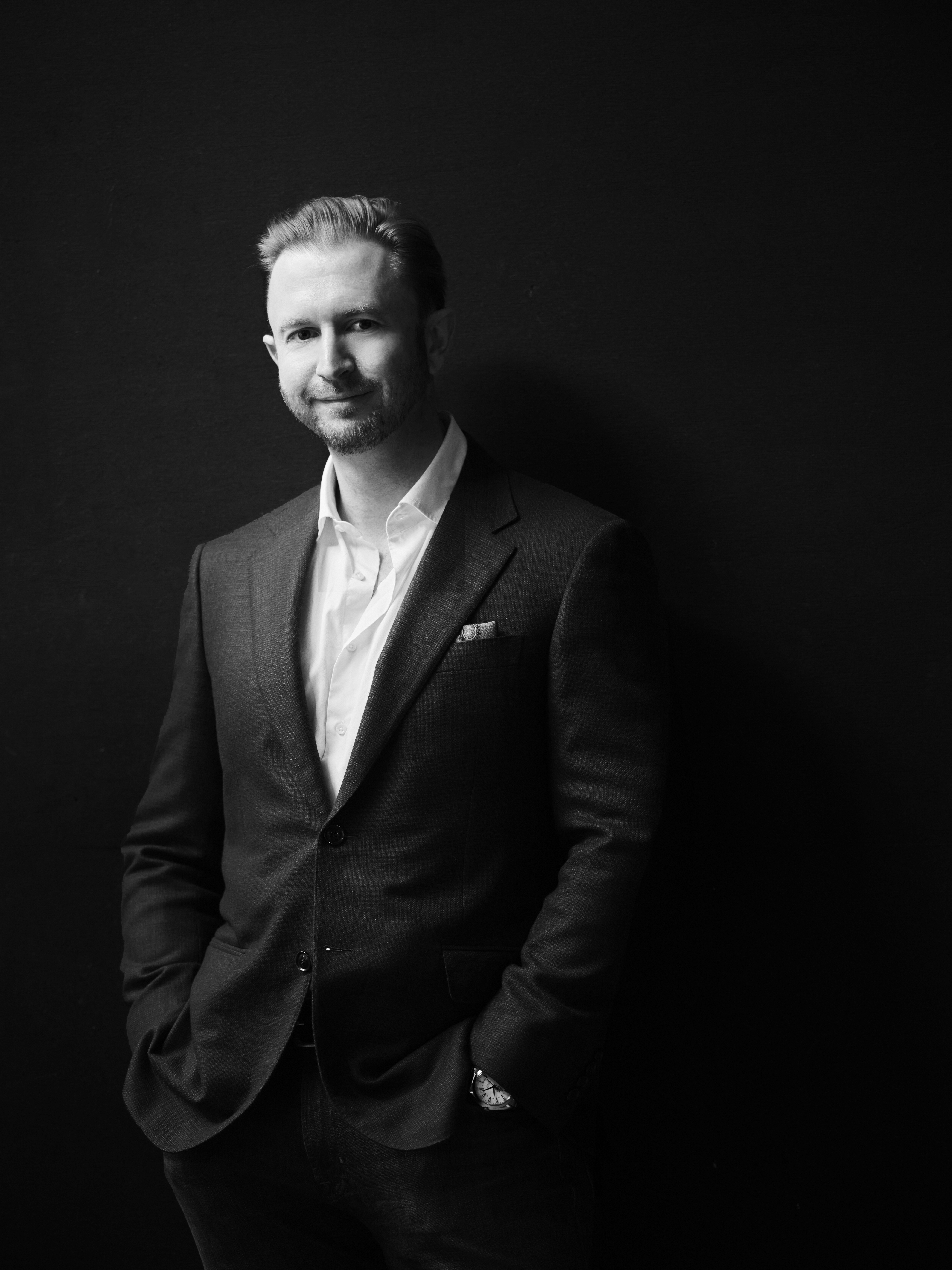 A professional man in a suit standing confidently against a dark background, conveying a sense of leadership and authority.